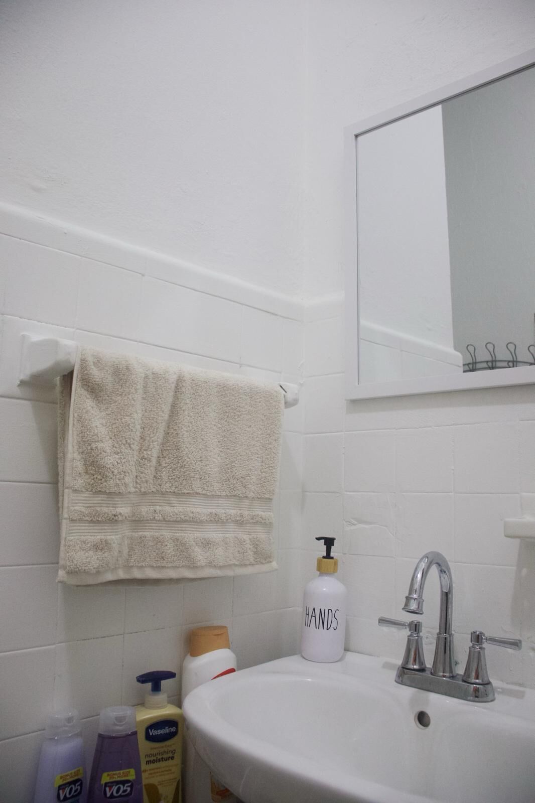Ein Badezimmer mit einem weißen Waschbecken, einem Spiegel darüber und Toilettenartikeln auf der Ablagefläche.