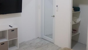 Una stanza con una TV a schermo piatto fissata al muro, una porta bianca, un armadio con ripiani e un tappeto di colore chiaro.