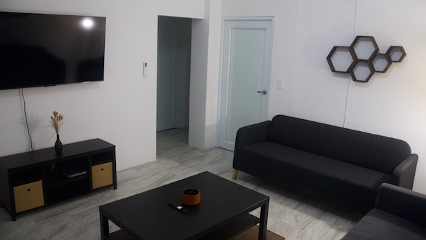 Un soggiorno moderno con una TV a schermo piatto, un divano nero, un tavolino da caffè e un elemento decorativo esagonale a parete.