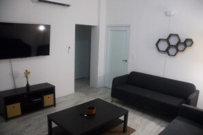 A modern living room with a flat-screen TV, a black sofa, a coffee table, and a decorative hexagonal wall piece. - Unit 2 Cozy Apartment with walking distance from bars, restaurants and beach (San Juan)