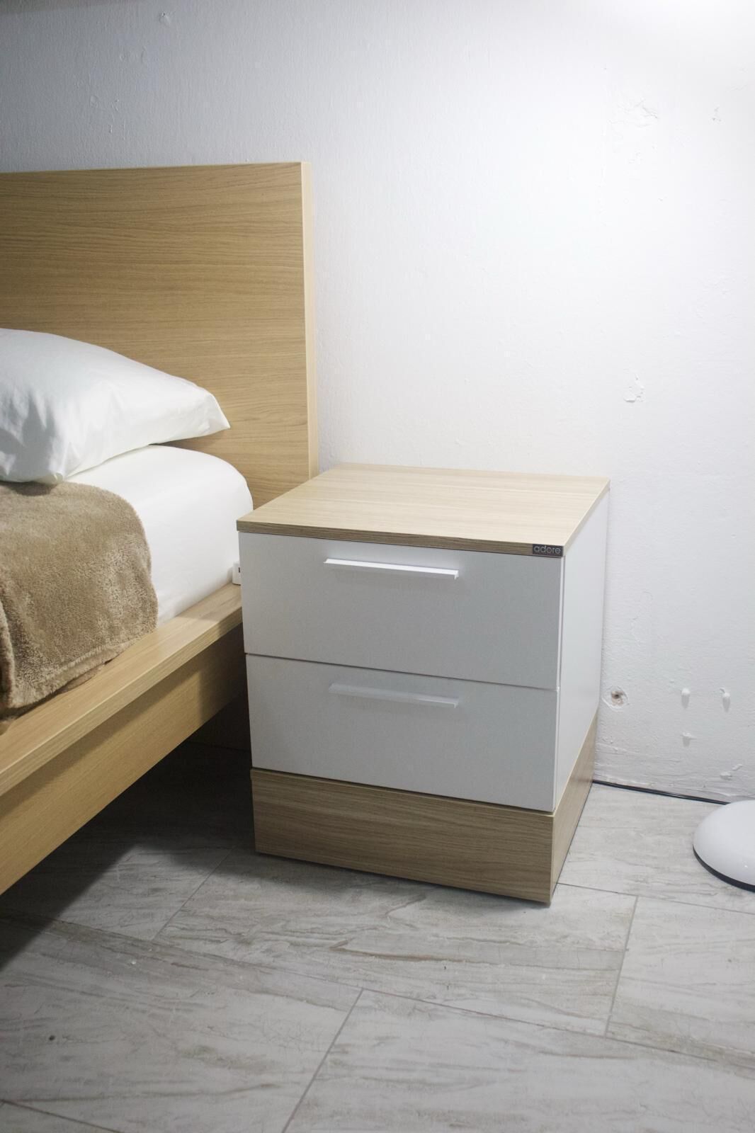 Ein kleiner Nachttisch mit Schubladen, ein Bett mit weißer Bettwäsche und ein Holzkopfstück.