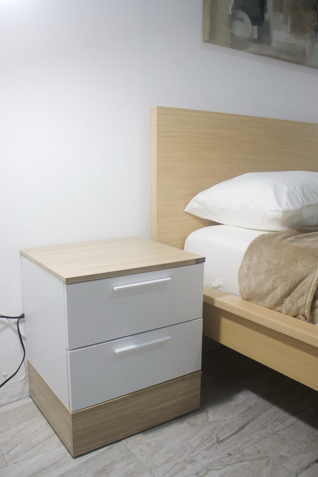 Une petite table de chevet avec des tiroirs, une tête de lit en bois et un lit avec une literie blanche et une couverture beige.