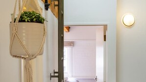 A narrow hallway with wooden flooring, a hanging macrame plant, and a bed in the adjacent room. - New York Loft | Private Car Park | Walk to Stadium (Christchurch)