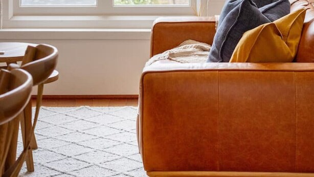 A room with a large window, a sofa with cushions, a floor lamp, and a dining area with chairs. - New York Loft | Private Car Park | Walk to Stadium (Christchurch)