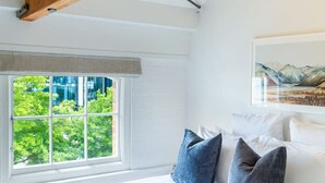 A bedroom with a large bed, a window with a view of greenery, and a wooden ceiling beam. - New York Loft | Private Car Park | Walk to Stadium (Christchurch)