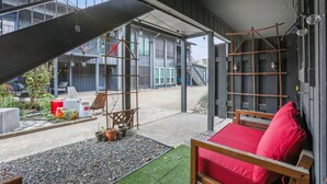 Un espacio exterior moderno con asientos, un cojín rojo, un columpio de madera y un pequeño jardín con plantas en macetas.