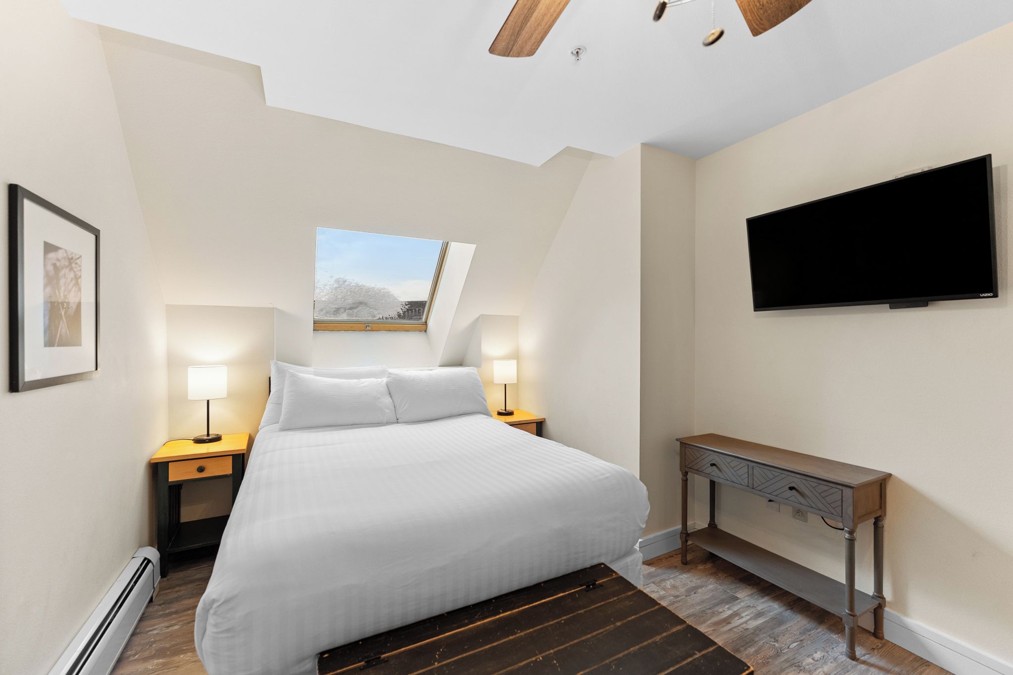 A bedroom with a bed, bedside lamps, a TV, a window, and a ceiling fan.