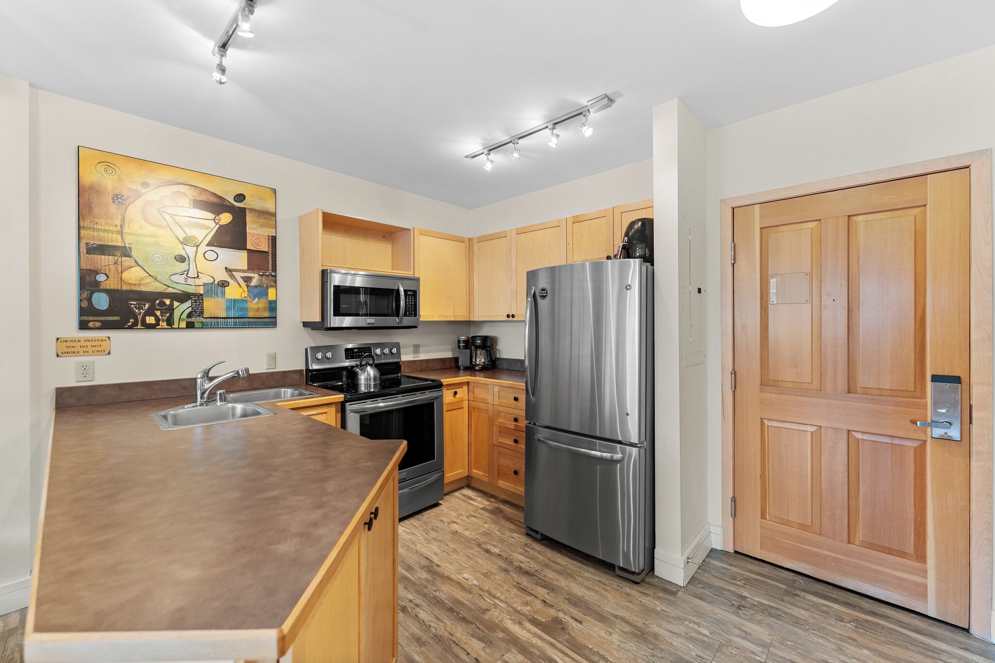 A modern kitchen with a stainless steel refrigerator, microwave, and stove, wooden cabinets, and a large island with a sink.