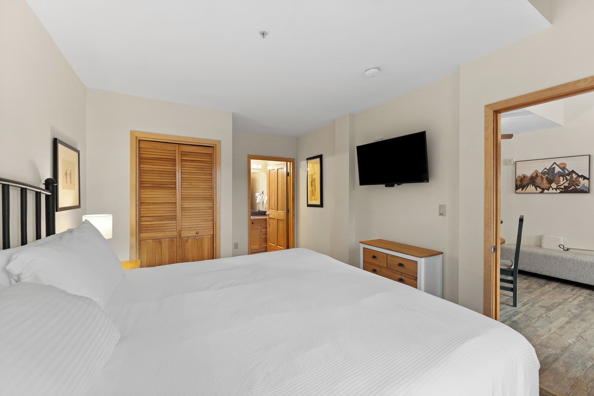 Un dormitorio con una cama grande, un armario de madera, un televisor montado en la pared y una cómoda de madera pequeña.