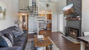 A spacious living room with a dark brown sofa, a wooden coffee table, and a fireplace. A staircase leads to an upper level with a view of the kitchen. - Beautiful 3-bedroom apt Skiview drive, 10 minutes to Gatlinburg (Gatlinburg)