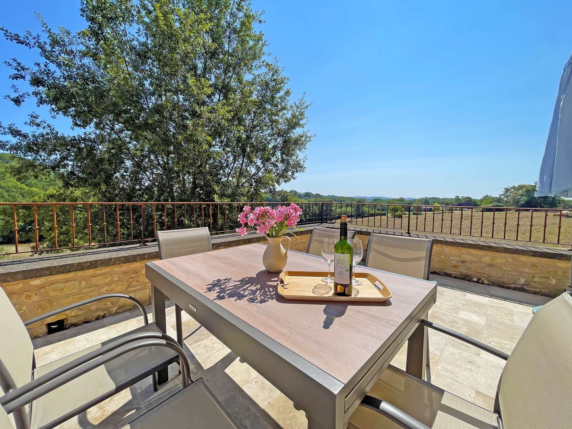 An outdoor dining area with a table, chairs, a bottle of wine, and a vase of flowers.
