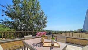 Zona pranzo all'aperto con tavolo, sedie, una bottiglia di vino e un vaso di fiori.
