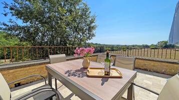 An outdoor dining area with a table, chairs, a bottle of wine, and a vase of flowers.