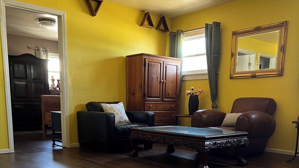 A living room with a wooden floor, a dark brown leather sofa, a wooden cabinet, and a large mirror on the wall. - A cosy space Hollywood unit with walking distance to Sunset Blvd (Los Angeles)