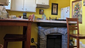 A kitchen with yellow walls, white cabinets, a stone fireplace, and a wooden dining table. - A cosy space Hollywood unit with walking distance to Sunset Blvd (Los Angeles)