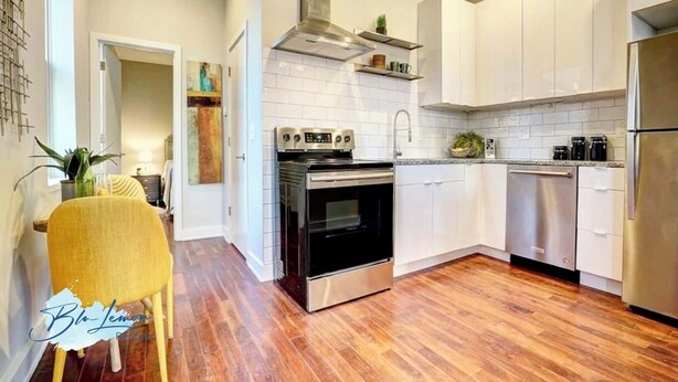 A modern kitchen with white cabinets, stainless steel appliances, and a wooden floor.