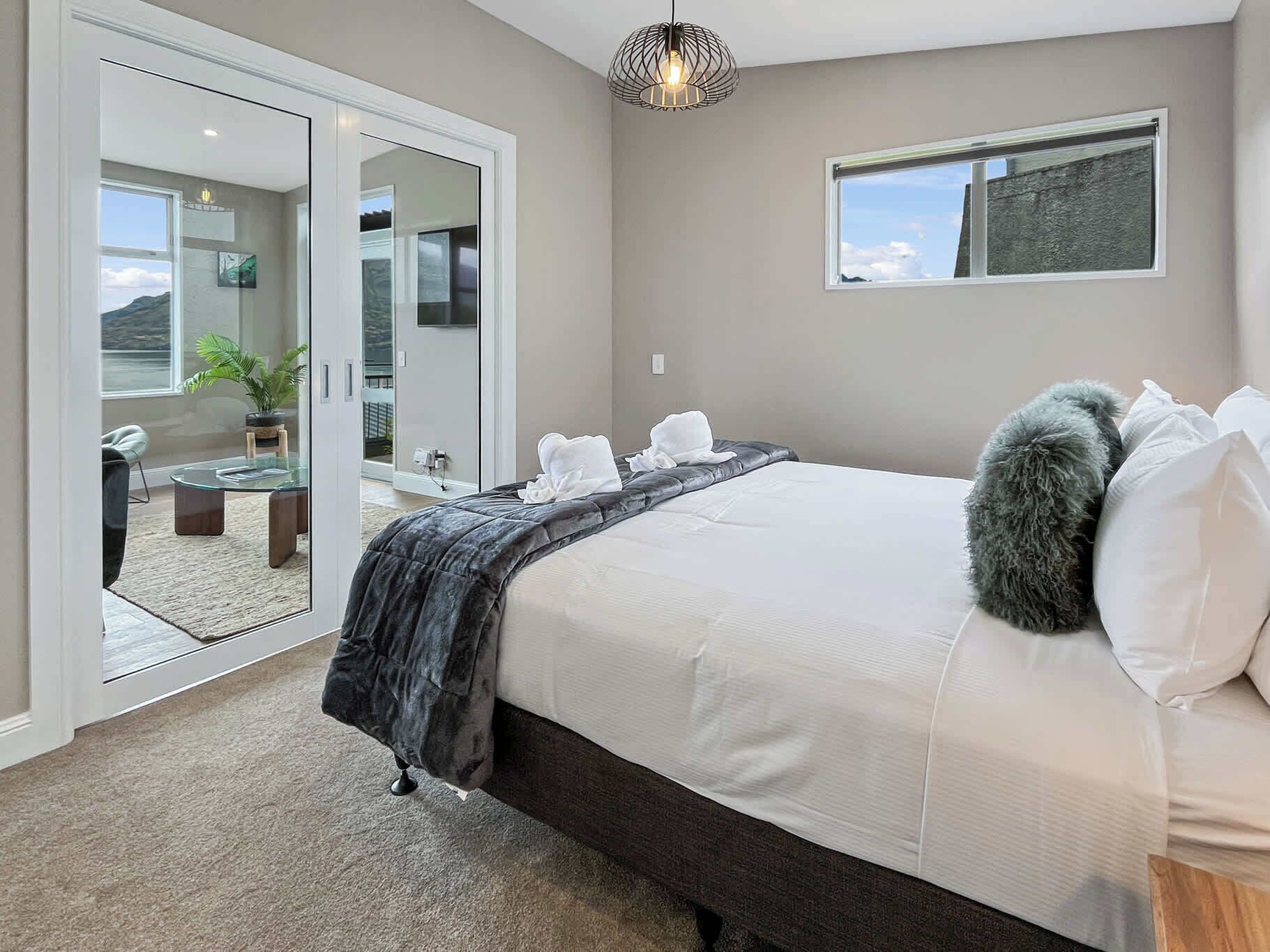 A modern bedroom with a large bed, a glass door leading to a balcony, and a view of the outdoors.