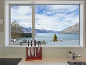 A kitchen with a large window overlooking a lake and mountains, a knife block, and a sink. - Chic Central Queenstown Retreat- Newly Renovated (Queenstown)