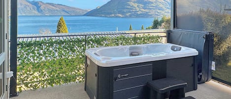 A balcony with a hot tub, a small stool, and a view of a lake and mountains.