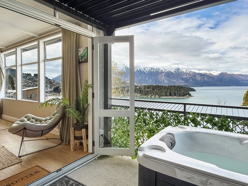 Un balcón con un jacuzzi, una silla y vistas a montañas y un lago.