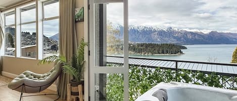 A balcony with a hot tub, a chair, and a view of mountains and a lake.