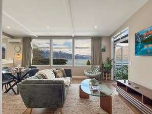 A modern living room with a sofa, a glass coffee table, and a view of mountains through large windows. - Chic Central Queenstown Retreat- Newly Renovated (Queenstown)