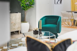A modern living room with a teal armchair, a glass coffee table, and a white cabinet.