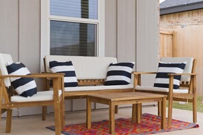 A wooden outdoor seating area with a sofa and chairs, a small table, and a colorful rug.