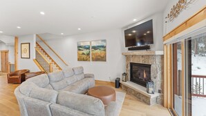 A modern living room with a sectional sofa, a fireplace, a TV mounted on the wall, and a staircase leading to another level. - A736-3 (Keystone)