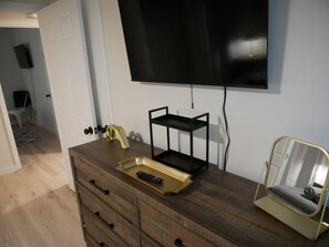 Ein modernes Wohnzimmer mit einem Holzkabinett, einem an der Wand montierten schwarzen Fernseher, einem kleinen schwarzen Regal und einem goldfarbenen Dekoartikel auf dem Kabinett.
