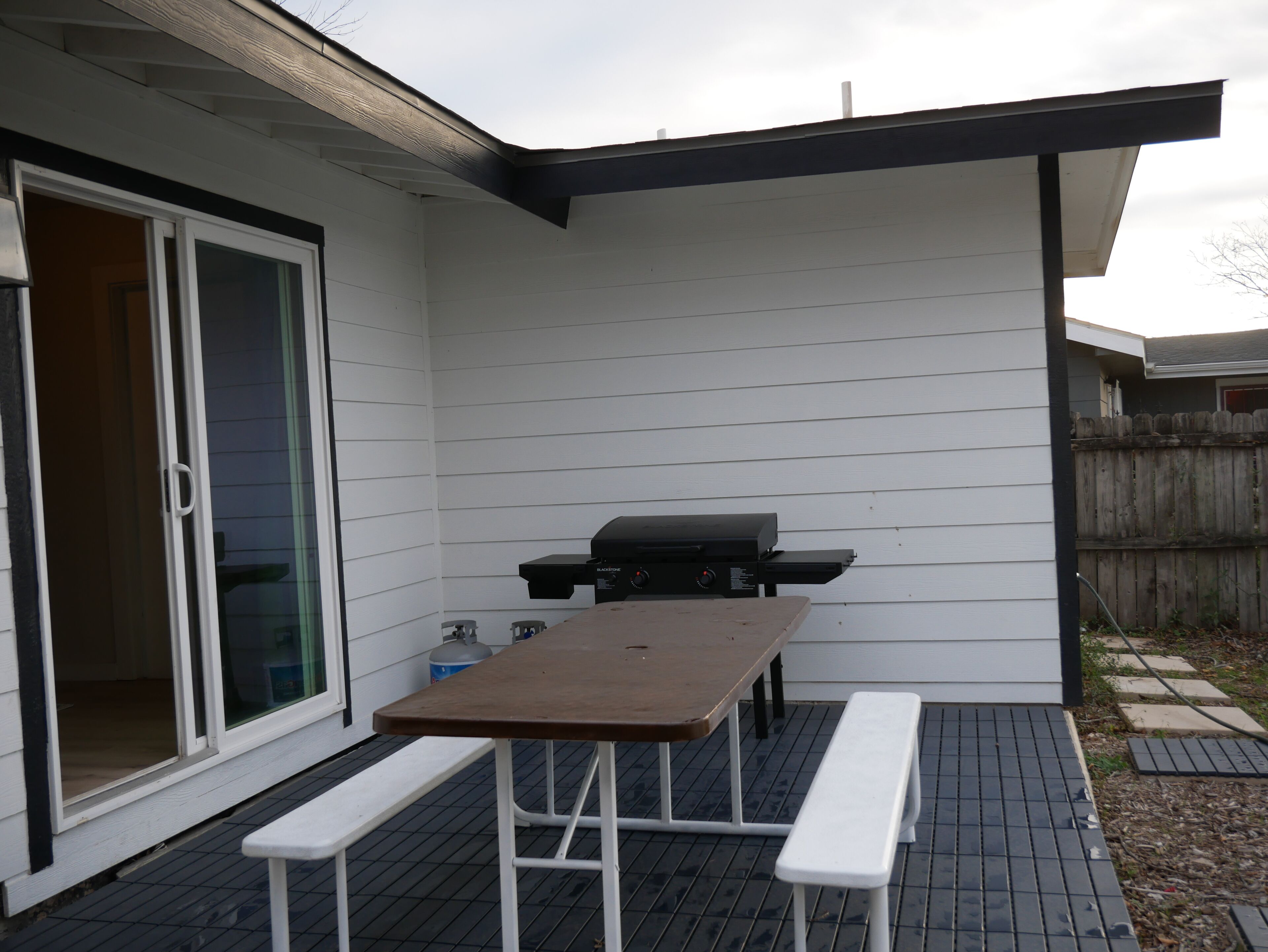 Un patio con mesa, bancos, una parrilla y una puerta corrediza de vidrio.