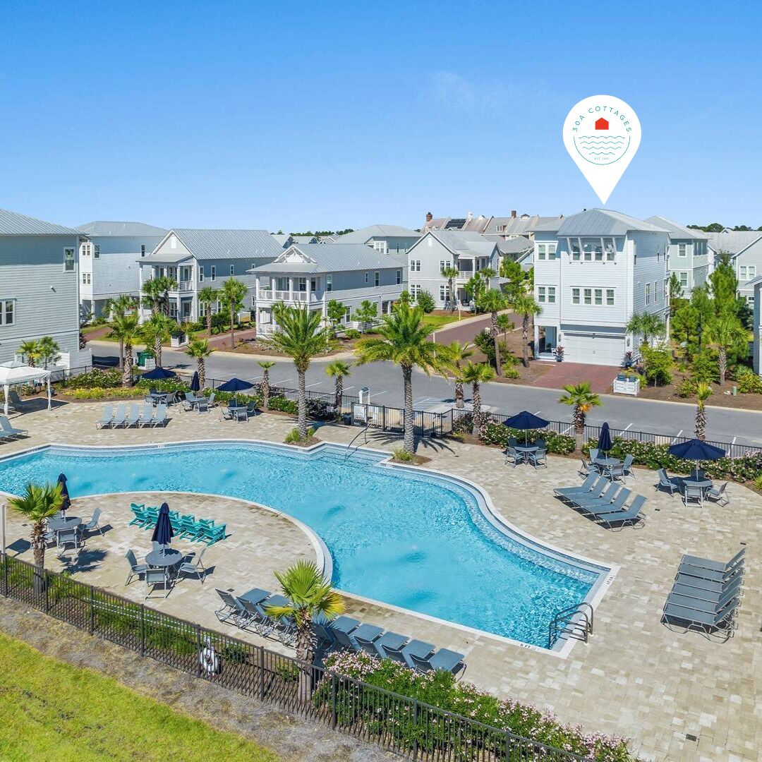 A pool area with lounge chairs and umbrellas, surrounded by a row of townhouses.