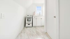 A narrow hallway with a white oven and cabinets, a window with a view, and a door. - Elegant Hideaway with Free Parking (White Plains)
