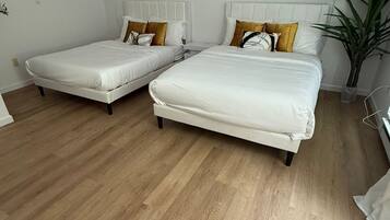 A modern hotel room with two single beds, wooden flooring, and a potted plant.