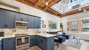 Una cocina moderna con armarios azul oscuro, un microondas y un horno. Hay un rincón comedor con un sofá azul y una mesa de centro de vidrio.