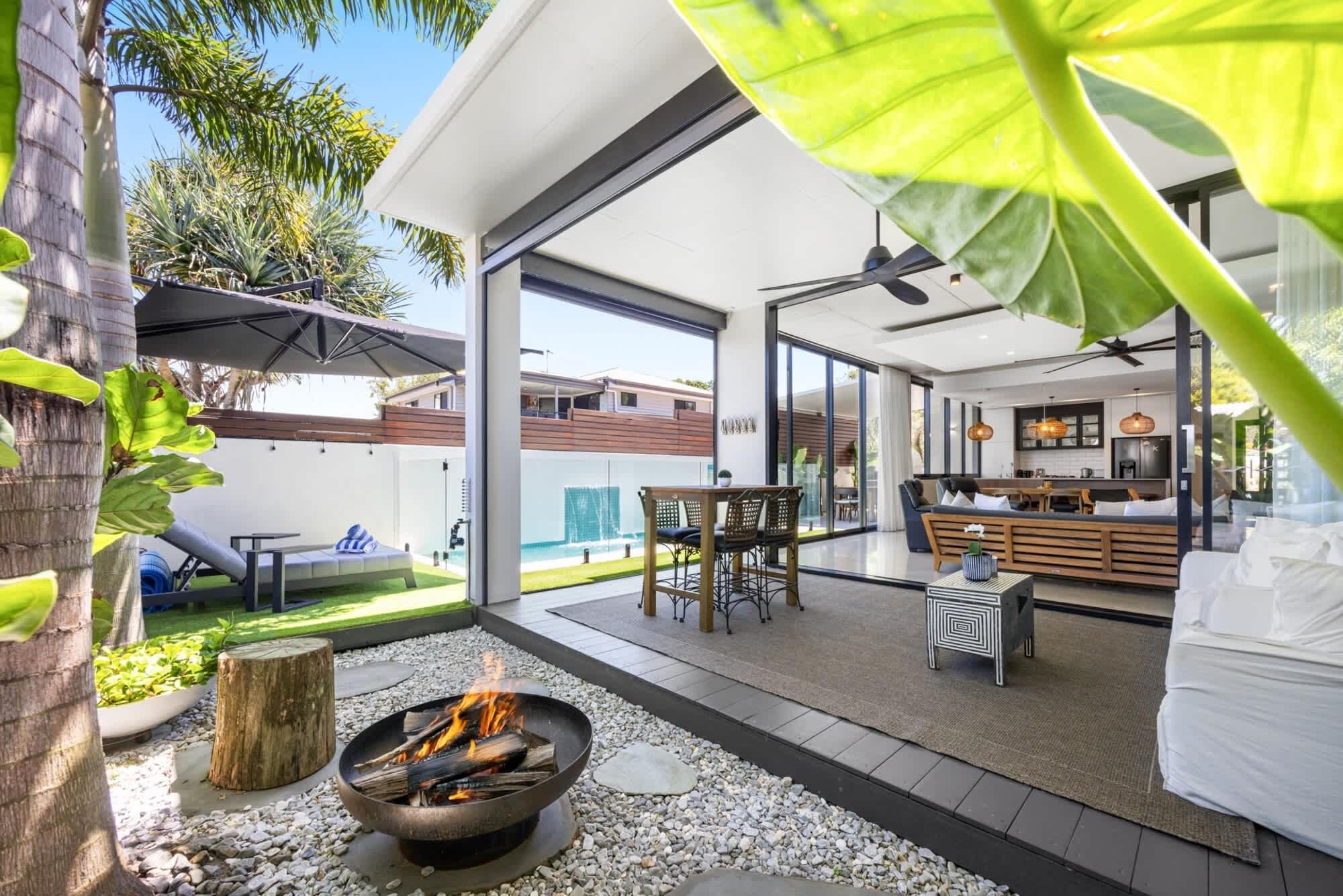 A modern outdoor living area with a fire pit, seating, and a view of the adjacent kitchen and dining area.