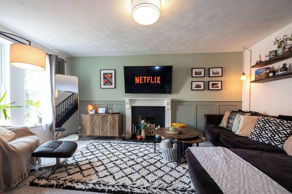A living room with a fireplace, a television mounted on the wall, and a staircase leading to another level. - Cosy Home in the Heart of Whitefield (Manchester)