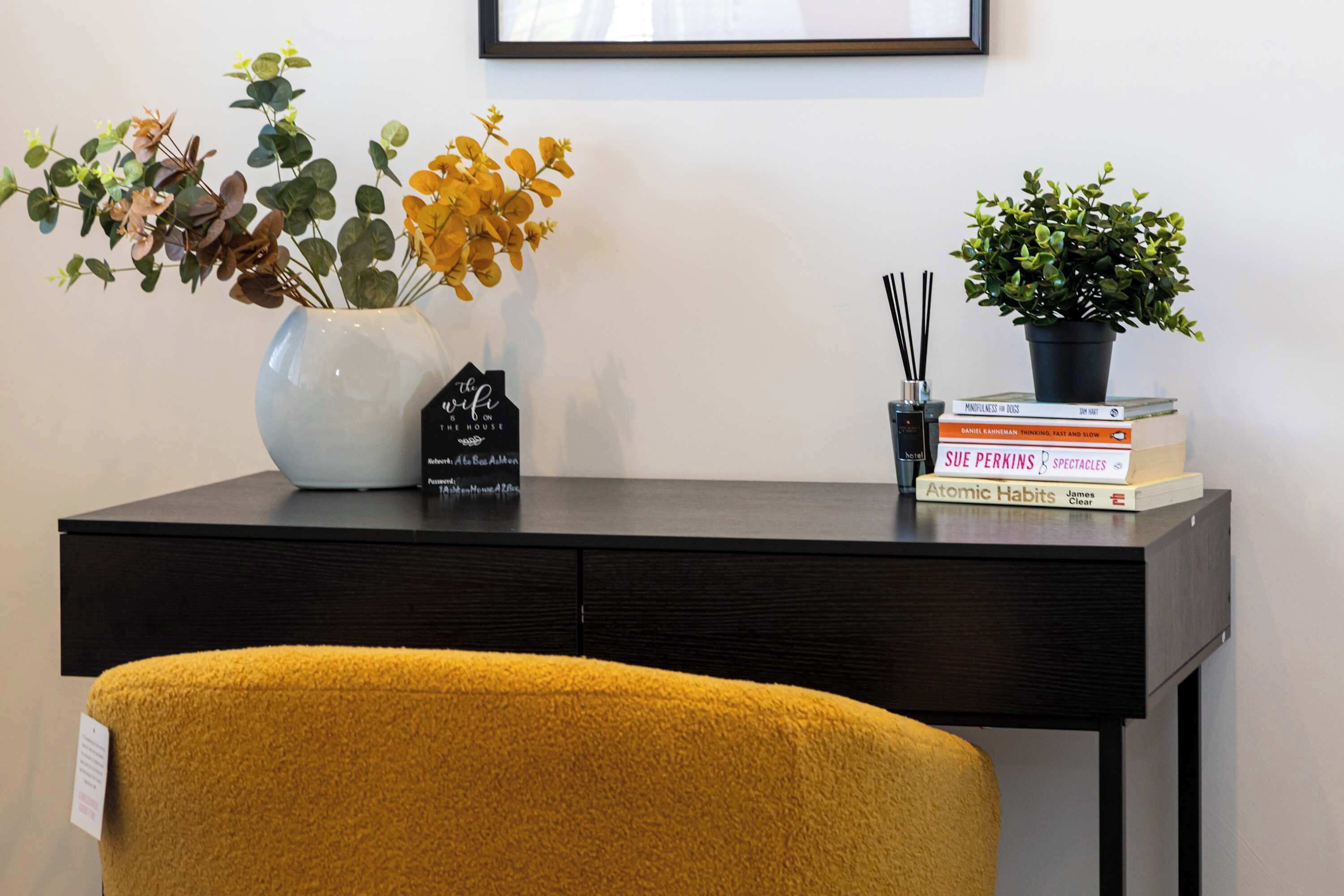 Een bureau met een bloevas, een klein bordje in de vorm van een huis en een stapel boeken.
