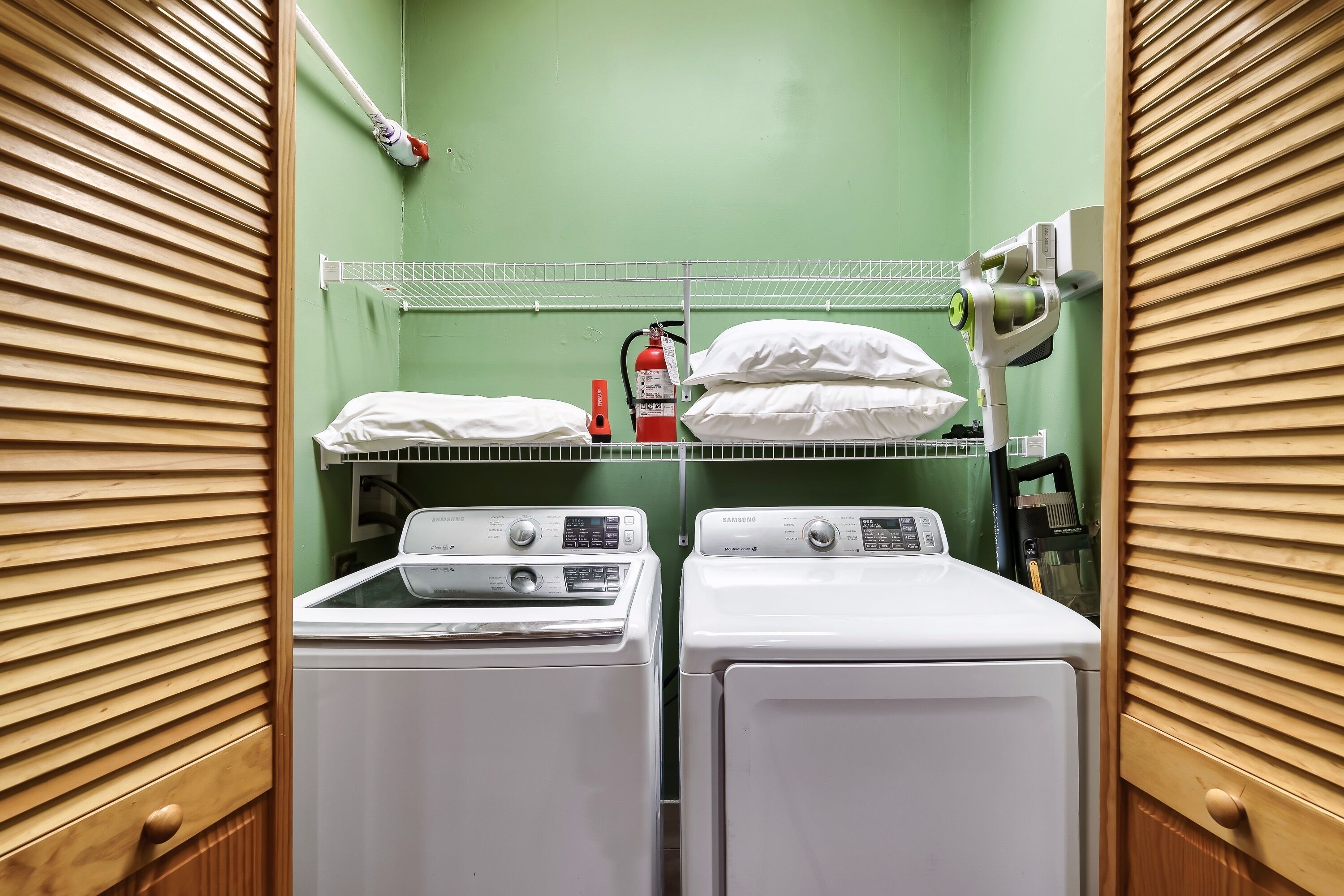 Une buanderie équipée de deux machines à laver et deux sèche-linge blancs, d’un extincteur et d’un appareil fixé au plafond.