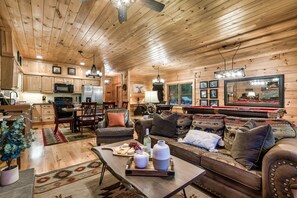 L’intérieur chaleureux d’un chalet avec des murs en bois, un coin repas, un salon doté d’un canapé et de coussins, et une table de billard.