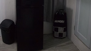 A compact room with a black refrigerator, a trash bin, a laundry bag, and a door. - Unit 1 Cozy Apartment with walking distance of bars, restaurant and beach (san juan)