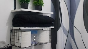 A bathroom with a shower curtain, a towel rack, and a shelf with plants and toiletries. - Unit 1 Cozy Apartment with walking distance of bars, restaurant and beach (san juan)