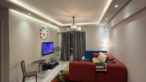 Ein modernes Wohnzimmer mit einem roten Sofa, einem an der Wand montierten Fernseher, einem Esstisch mit Stühlen und einer Chandelier.