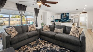 A modern living room with a grey sectional sofa, a ceiling fan, and a view of the kitchen and pool. - Beautiful 3BR/2BA - Steps from the Gulf & FREE Boat ramp - Kayaks & bikes incl. (Hernando Beach)