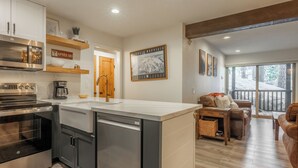 A modern kitchen with built-in appliances, a central island, and a dining area with a view of the outdoors. - Chamonix 35: Beautiful Upgrades, Walk to Lifts (Mammoth Lakes)