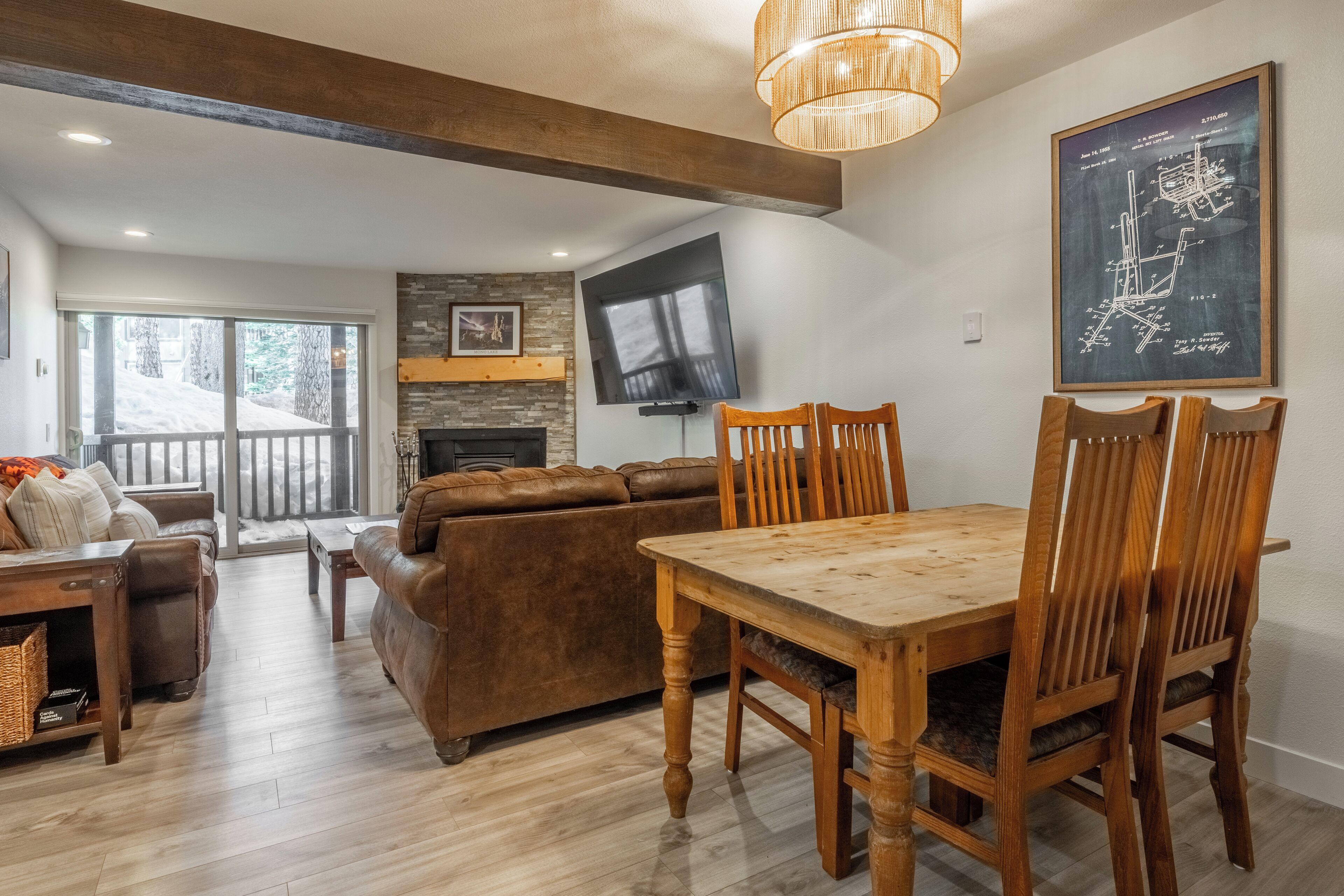 A modern living room with a fireplace, a dining area with wooden furniture, and a large window overlooking a snowy landscape.