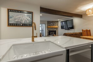 A modern kitchen with a white marble countertop, a built-in sink, and a wooden ceiling beam. - Chamonix 35: Beautiful Upgrades, Walk to Lifts (Mammoth Lakes)