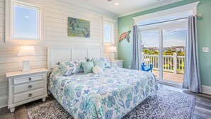 A bedroom with a bed, nightstands, a ceiling fan, and a view through a sliding glass door. - Top Sail Beach Sunsets (Sneads Ferry)