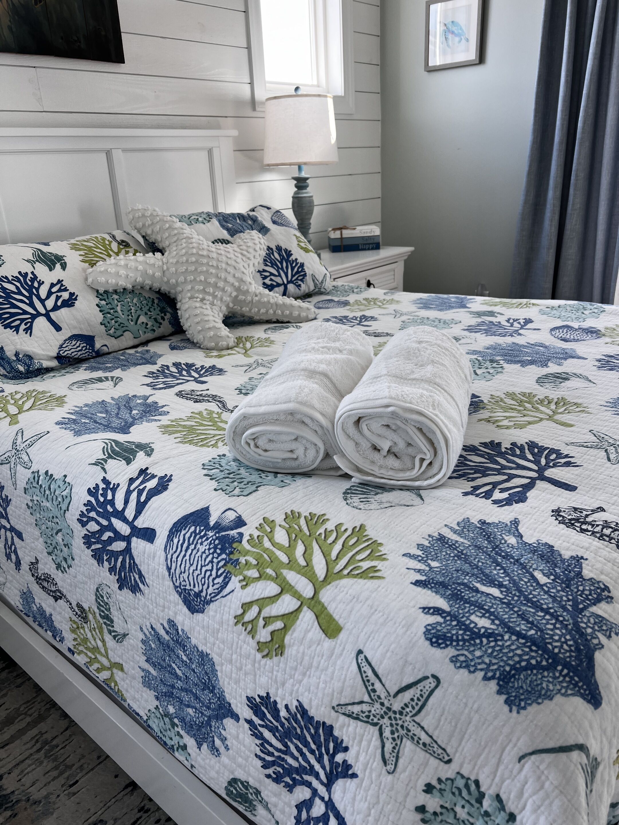 A neatly made bed with a floral bedspread, a white pillow, and a starfish pillow.