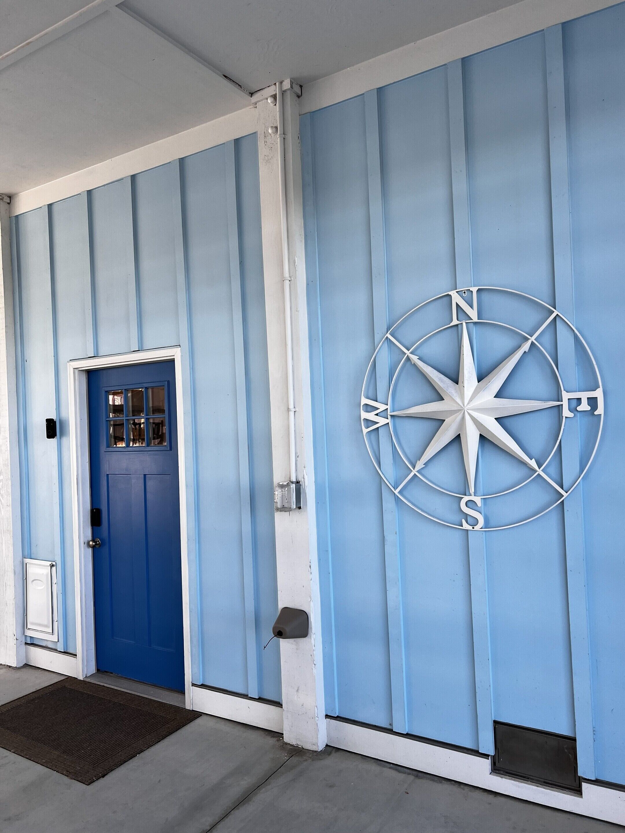 A blue door with a window, a white mailbox, and a compass on the wall.